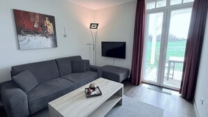 A modern living room with a grey sofa, a coffee table, a flat-screen TV, and a large window with curtains.