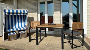 A patio with a striped chair, a wooden table, and two wooden chairs.