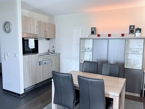 Une cuisine moderne avec un coin repas, comprenant une table et des chaises, une horloge et des appareils électroménagers intégrés.