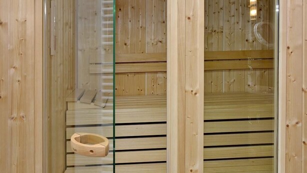A wooden sauna with a glass door and a wooden bench.