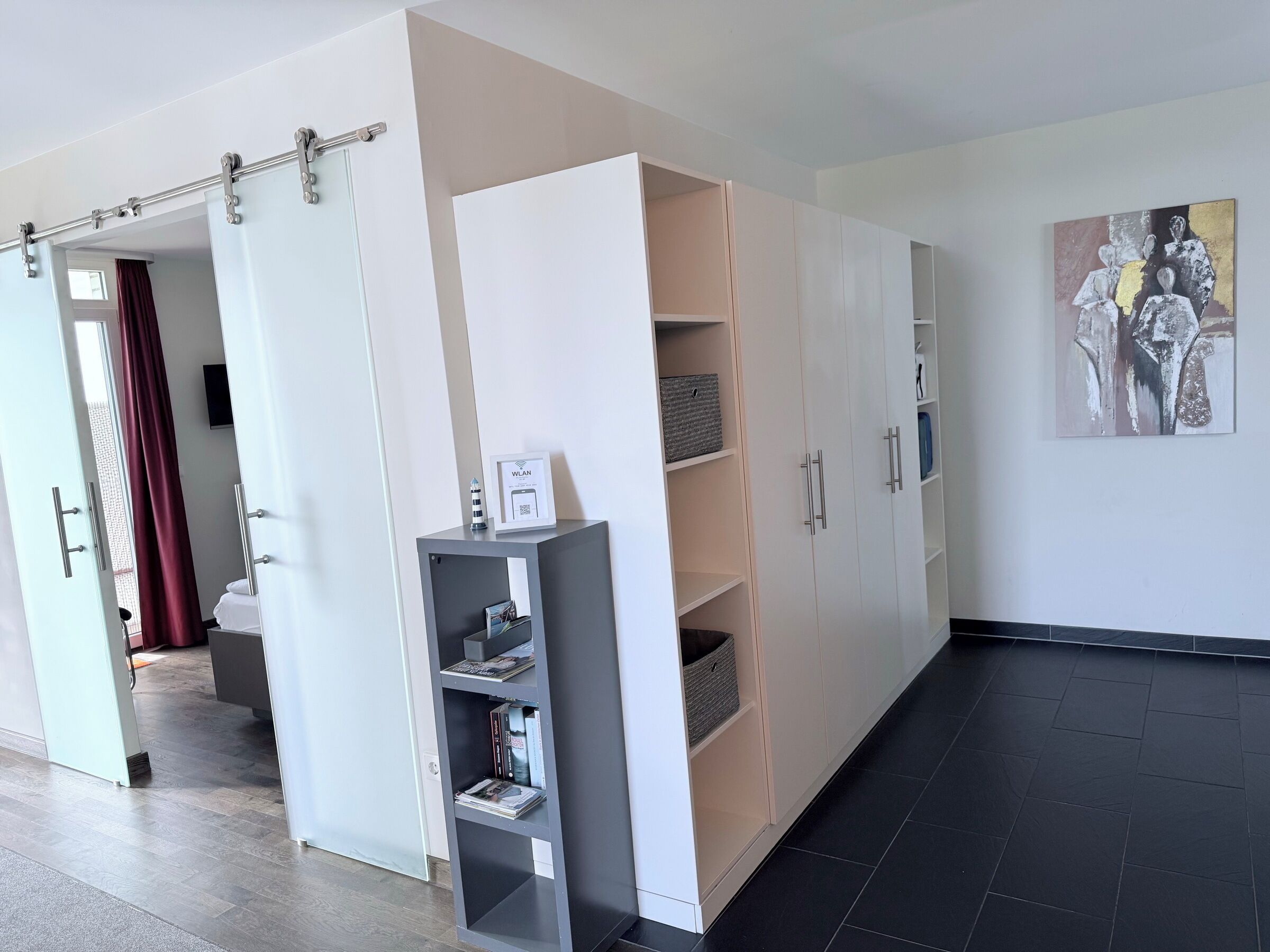 Une chambre d’hôtel moderne dotée d’une porte coulissante, d’une bibliothèque grise et d’une grande armoire.
