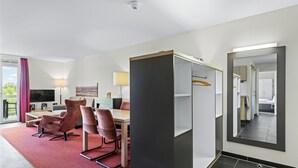 A hotel room with a dining area, a TV, a sofa, and a mirror.