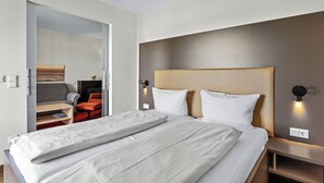 A modern hotel room with a large bed, a sofa, a small table, and a wall-mounted light fixture.