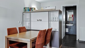 A modern kitchen with a dining table and chairs, a built-in cabinet with glass doors, and a visible bathroom with a sink and mirror.