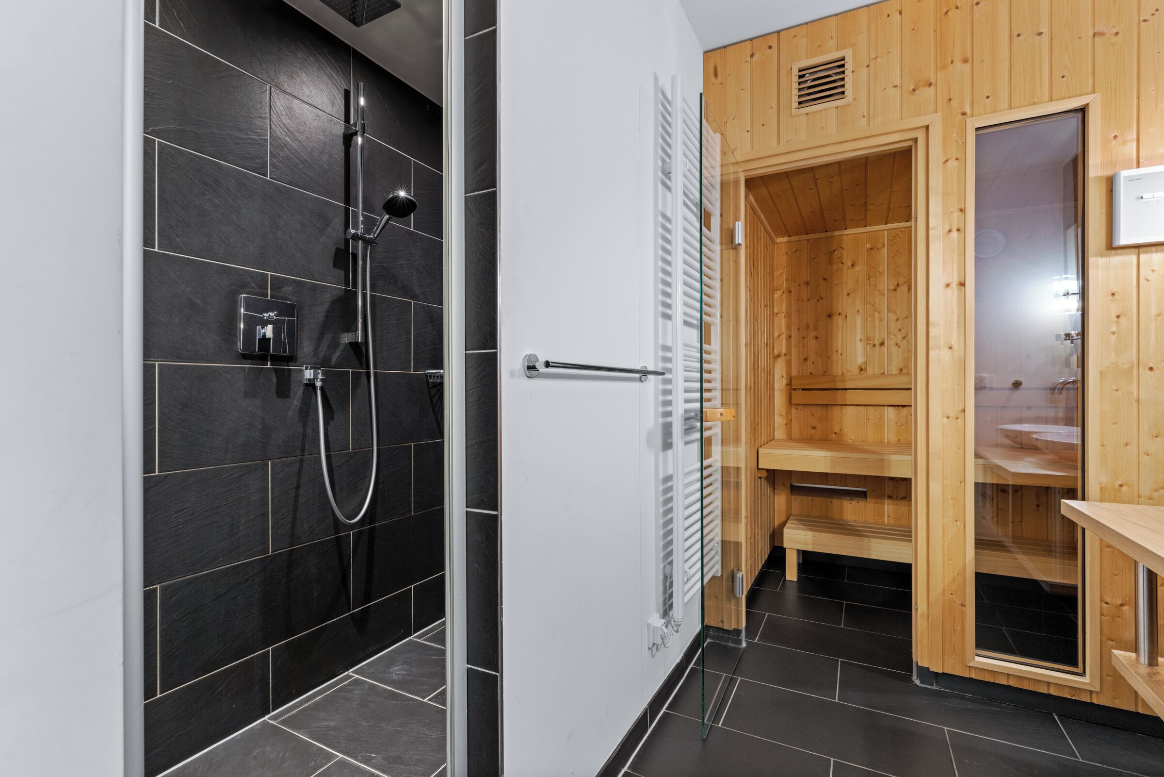 A modern bathroom with a shower, a wooden sauna, and a glass door.