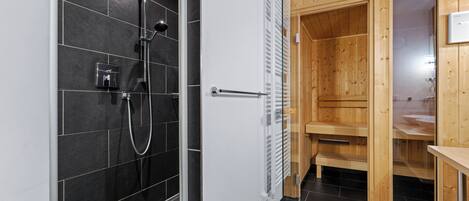 A modern bathroom with a shower, a wooden sauna, and a glass door.