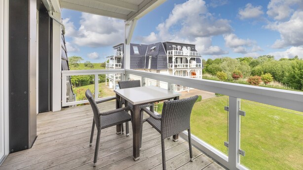 A covered outdoor area with a table and chairs, a view of a house, and a grassy landscape.