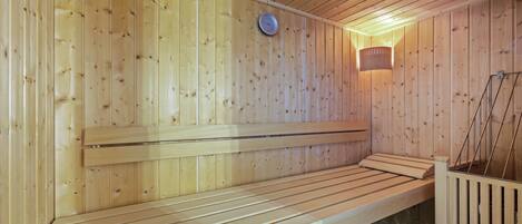A sauna with wooden walls and benches, a clock, and a wall-mounted light fixture.