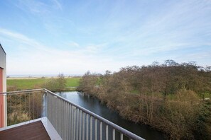 A balcony with a view of a river and trees. - Tolles Ferienapartment mit Balkon, Meerblick, Eigener Sauna und Whirlbadewanne (Nordseeheilbad Schillig)