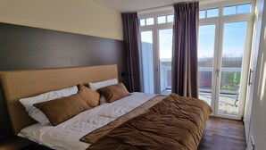 A bedroom with a large bed, a headboard, and a view through a glass door to the outside.