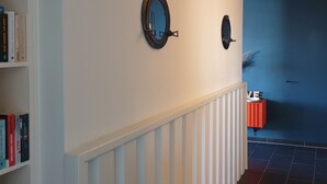 A hallway with a white railing, a blue wall, and two wall-mounted mirrors.
