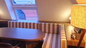 A cozy room with a wooden table, striped bench seating, a lamp, and a view through a skylight.