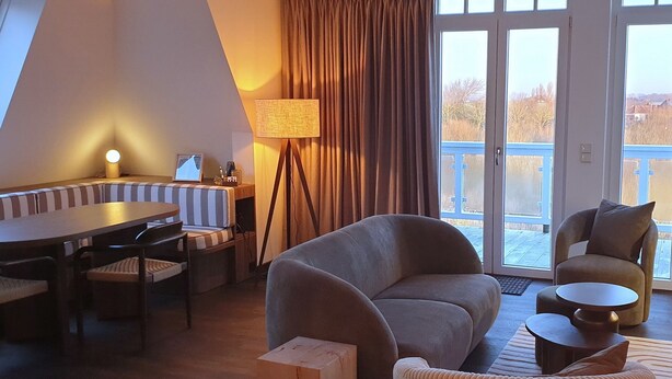 A cozy living room with a sofa, armchairs, a dining table, and a lamp.