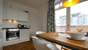 A modern kitchen with white cabinets, a wooden dining table, and a view of the city through large windows.