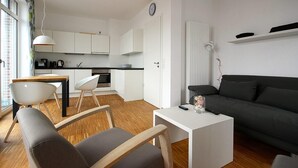 Una sala de estar moderna con un sofá, una mesa de comedor con sillas, una zona de cocina y una pared blanca con un reloj.