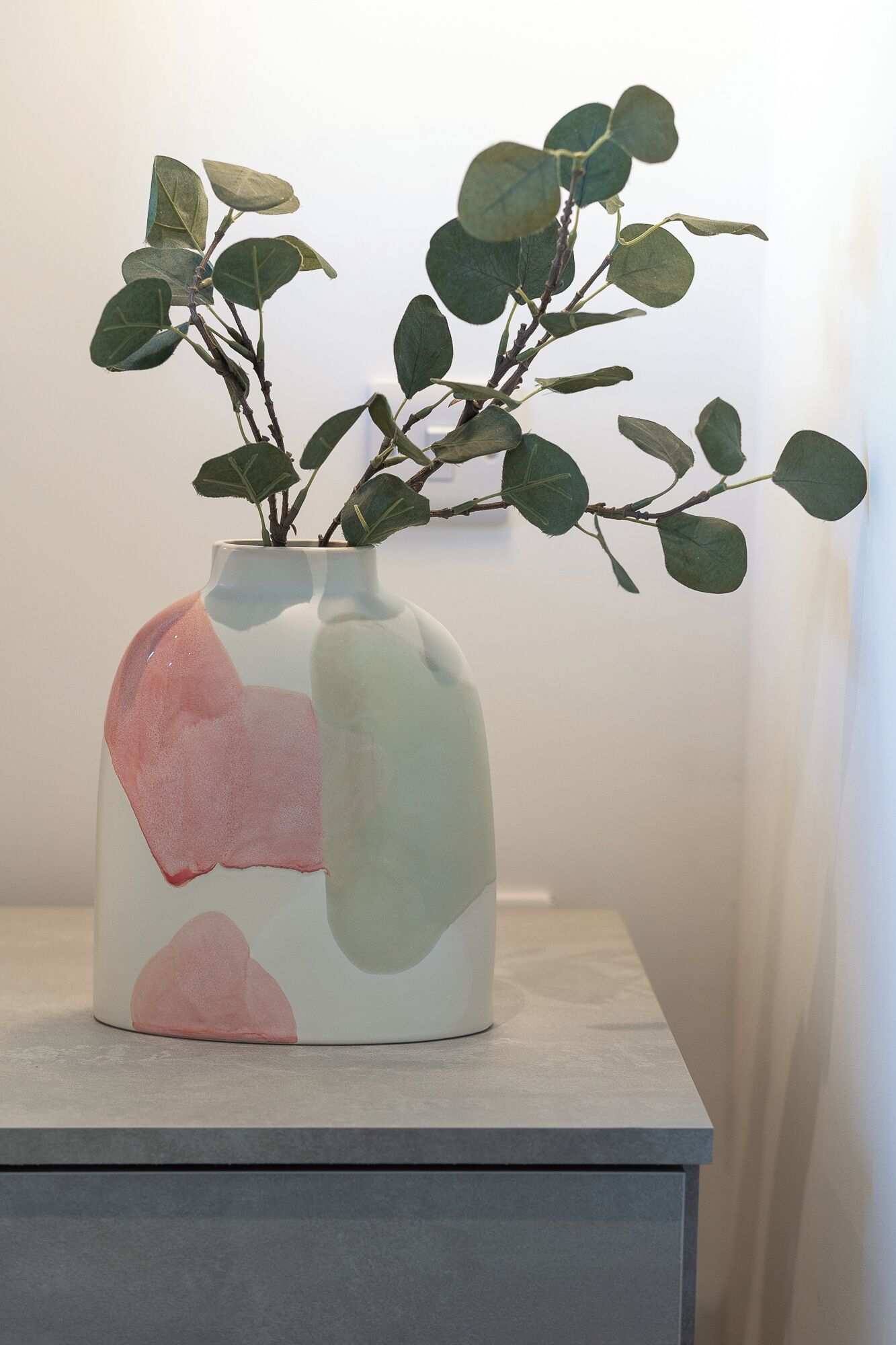 A vase with abstract design and a plant with green leaves.