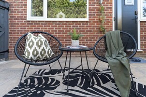 Two black wicker chairs with patterned cushions, a small table with a potted plant, and a green throw blanket draped over one chair.