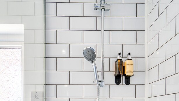 A modern bathroom with white subway tiles, a glass shower enclosure, a handheld showerhead, a wall-mounted faucet, and two bottles of lotion. - The Madison (Southampton)