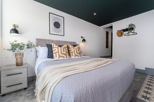 Un dormitorio moderno con una cama, mesitas de noche, una lámpara de pared y una obra de arte enmarcada.