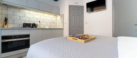 A compact bedroom with a bed, a wooden tray with bread, and a TV mounted on the wall.