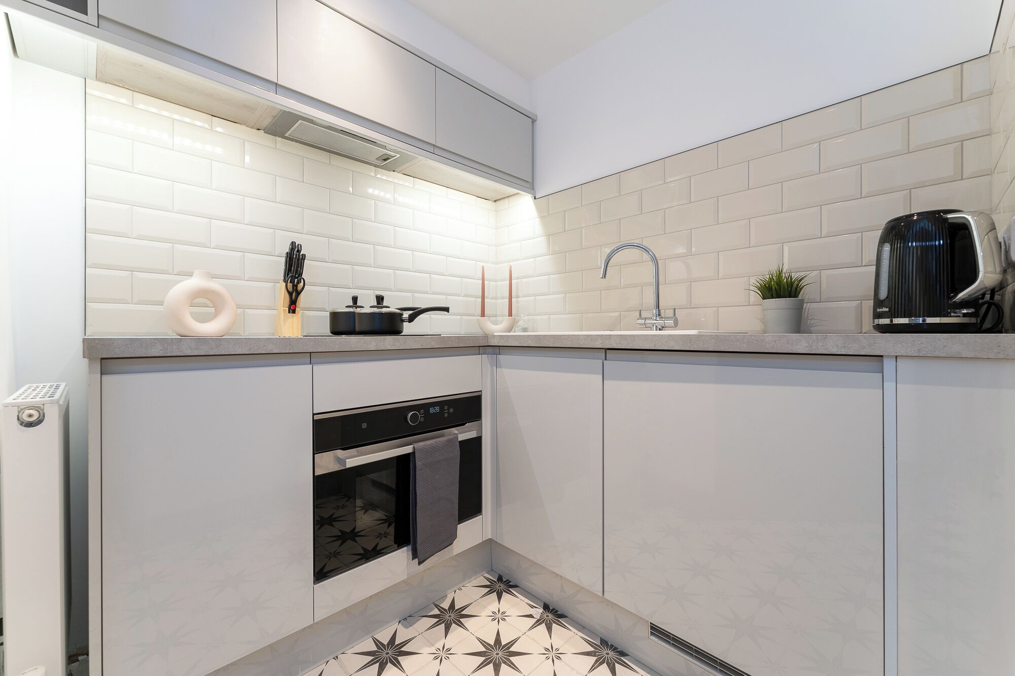 Una cocina moderna con armarios blancos, horno empotrado, cocina y hervidor sobre la encimera.