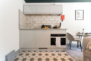 Una cocina compacta con salpicadero de azulejos, horno empotrado y un pequeño comedor con mesa y silla.