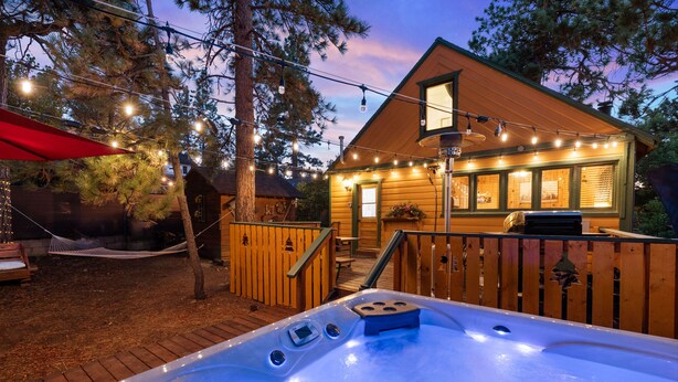 Una cabaña de madera con jacuzzi, luces colgantes y una hamaca.