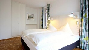 A bedroom with a bed, a wardrobe, a bedside lamp, and a window with curtains.