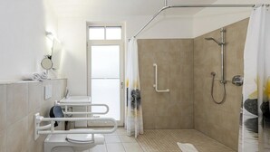 A modern bathroom with a walk-in shower, a toilet with a safety bar, and a sink.
