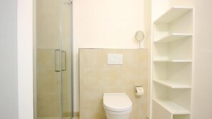 Un baño con cabina de ducha de vidrio, inodoro y dispensador de papel higiénico en la pared.