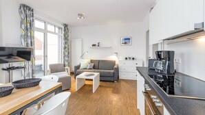 Un espacio habitable pequeño con kitchenette, un sofá, zona de comedor y televisión.
