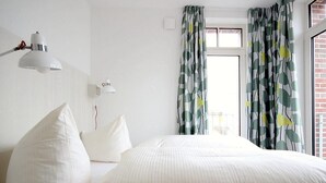 Habitación de hotel con cama, dos lámparas de noche, ventana con cortinas y vista a un edificio.