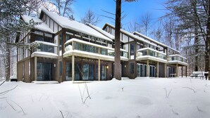 Un bâtiment moderne à plusieurs étages, doté de grandes fenêtres et d’un toit enneigé, entouré d’arbres.