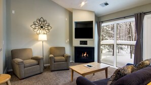 Un salon chaleureux avec deux fauteuils, un canapé, une cheminée et une grande fenêtre donnant sur un paysage enneigé.