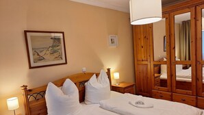 Een hotelkamer met twee bedden, houten hoofdeinden, een grote spiegel en een schilderij aan de muur.