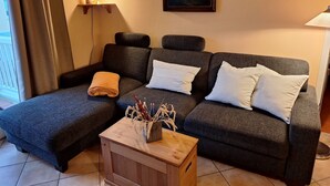Een gezellige woonkamer met een donkergrijze bank, een klein houten bijzettafeltje met een vaas, en een schilderij van een zeilboot aan de muur.