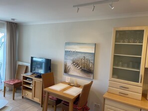 Una sala de estar con televisor, una mesa de comedor con sillas, un cuadro en la pared y un aparador.