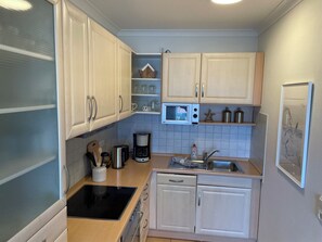 Una cocina con armarios blancos, microondas, cafetera y lavamanos.