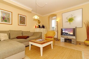 Un soggiorno con divano, poltrona, tavolino, televisore e opere d'arte alle pareti.