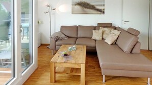 Una sala de estar moderna con un sofá seccional marrón, una mesa de centro de madera y un ventanal grande.