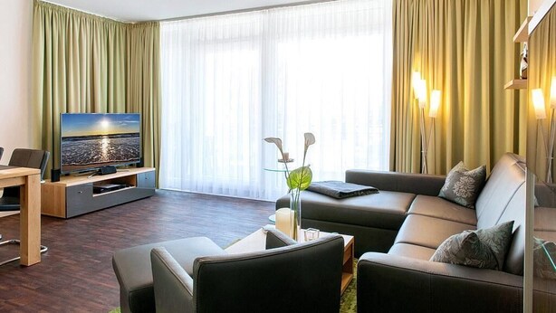 Ein modernes Wohnzimmer mit einer Couch, einem Couchtisch und einem Fernseher auf einem Standfuß.