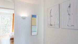 A hallway with a bed, a wall-mounted light, and three framed artworks.