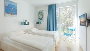 A bedroom with two beds, a window with curtains, a chair, and artwork on the walls.