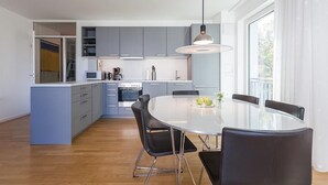 A modern kitchen with grey cabinets, a central island, and a dining area with a round table and black chairs.