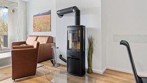 Una sala de estar moderna con un estufa de leña negra, un sofá de cuero marrón y un ventanal con vistas a un campo.