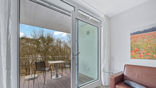 Una habitación con puerta de vidrio corredera que da a una terraza exterior con mesa y sillas.