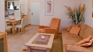 A living room with a beige sofa, a matching armchair, a small coffee table, and a dining area with a table and chairs.