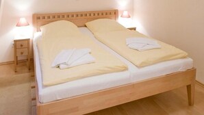 A double bed with two pillows and a blanket, a bedside table with a lamp, and a small drawer.