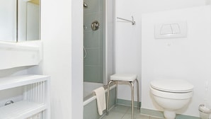 Un baño con inodoro blanco, ducha con puerta de vidrio, lavamanos blanco y espejo.