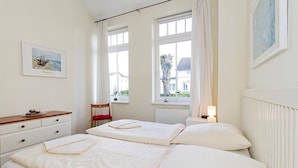 Un dormitorio con dos camas, un aparador de madera, una silla y una ventana con vistas a casas.